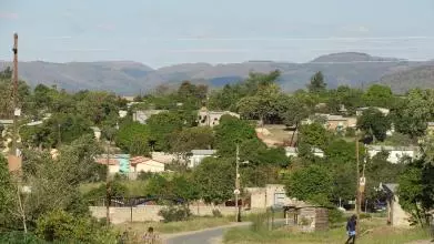 A scene of a rural south african town with overhead power cables and mountains in the background. A road runs through the middle.