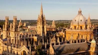 An image of the Radcliffe Camera and All Soul's College taken from rooftop level. The buildings are lit up by golden hour sunlight, against a blue sky. ©OUImages /Whitaker studio