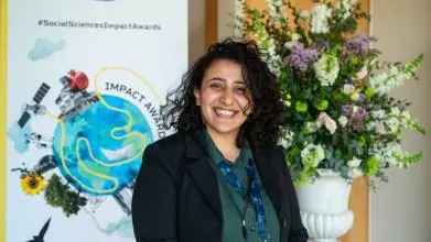 Dr Mona Ibrahim smiles to camera. In the background is the Impact Awards branding and a flower arrangement.