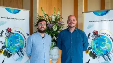 Alessio Bertolini and Jonas Valente smile to camera. In the background is the Impact Awards branding and a flower arrangement.