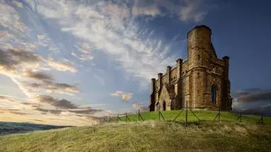 A historic chapel sits atop a hill with sunset in the background