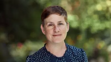 Prof Kathryn Eccles has a short pixey hair cut, wearing a dark blue top, smiling at the camera. 