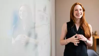 Female academic standing next to a whiteboard smiling and holding a pen 