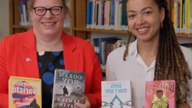 Dr Velda Elliott and Dr Zaahida Nabagereka sit side by side, smiling and holding books by authors of colour