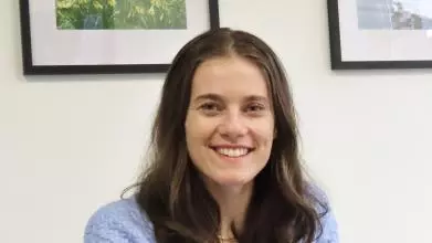 Faith Inch has shoulder length brown hair, wearing glasses smiling at the camera.