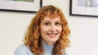 kate oconnor, ha shoulder length red hair, wearing a blue top smiling at the camera.