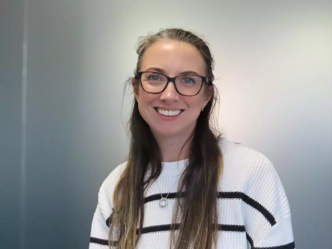 Sophie has long brown hair. She is wearing large round glasses and a white jumper with thin black stripes