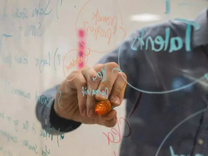 A hand writing on a glass wall with coloured felt tips