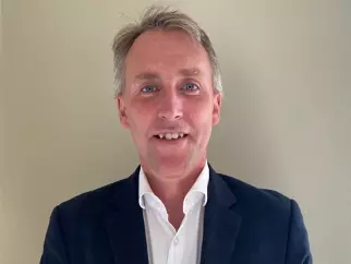 Professor Martin has short grey hair. He is wearing a white shirt and dark blazer. 