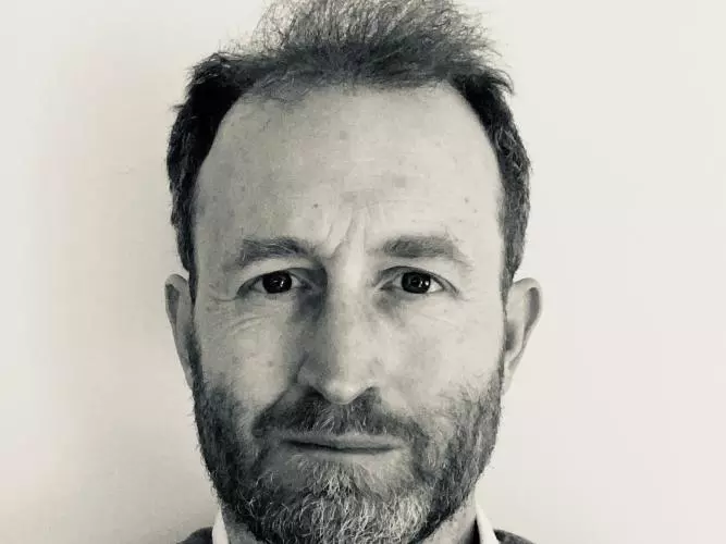 A black and white photo of Dr Hodgetts. He has short hair and is wearing a dark jumper and white shirt.