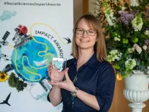 Dr Jennifer Seddon smiles and holds her prize trophy. In the background is the Impact Awards branding and a flower arrangement.