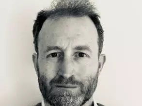 A black and white photo of Dr Hodgetts. He has short hair and is wearing a dark jumper and white shirt.