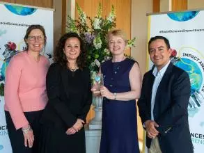 Four Young Lives team members smile and hold the Developing Impact trophy. In the background is the Impact Awards branding and a flower arrangement.