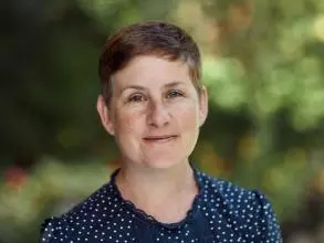 Prof Kathryn Eccles has a short pixey hair cut, wearing a dark blue top, smiling at the camera. 