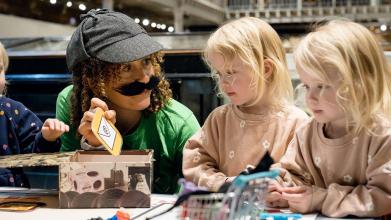 A researcher dressed up as a detective shows two young children an email symbol 