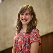 Woman with medium length brown hair and red patterned top smiles in front of camera