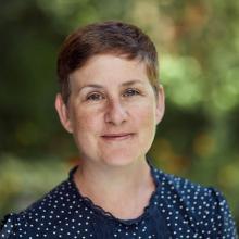Prof Kathryn Eccles has a short pixey hair cut, wearing a dark blue top, smiling at the camera. 