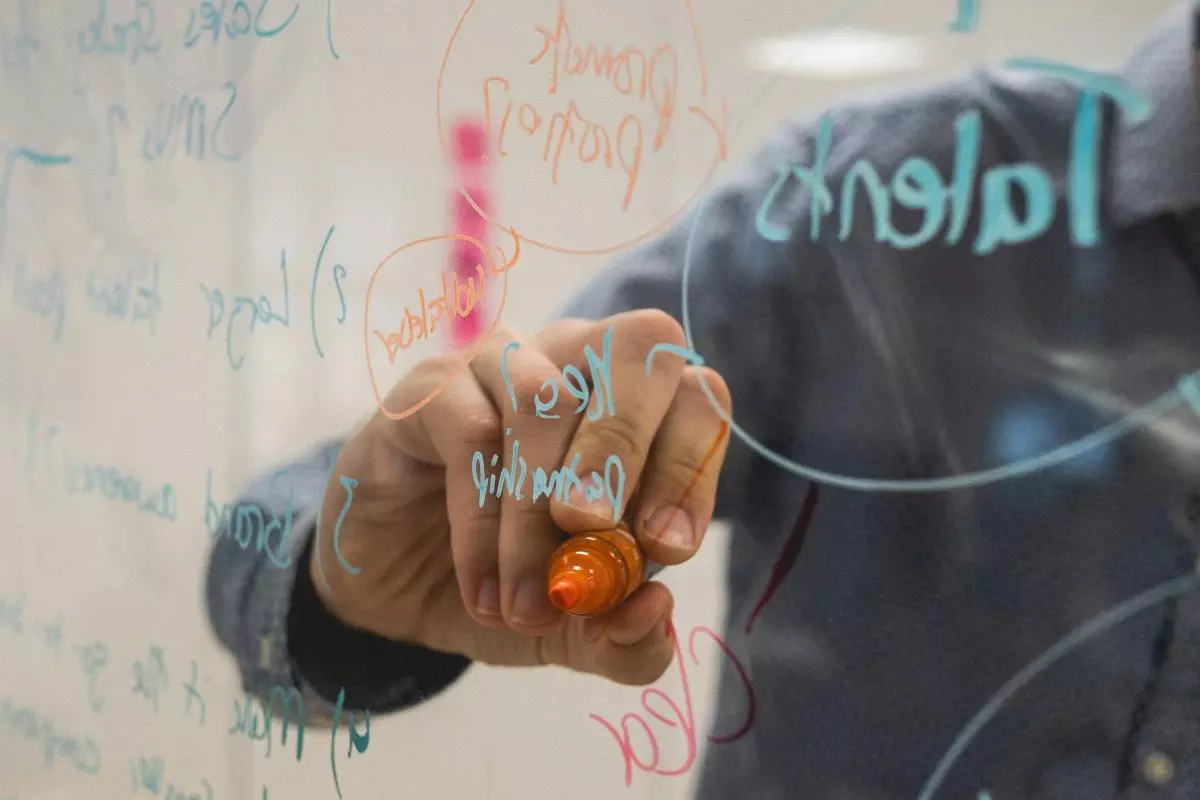 A hand writing on a glass wall with coloured felt tips