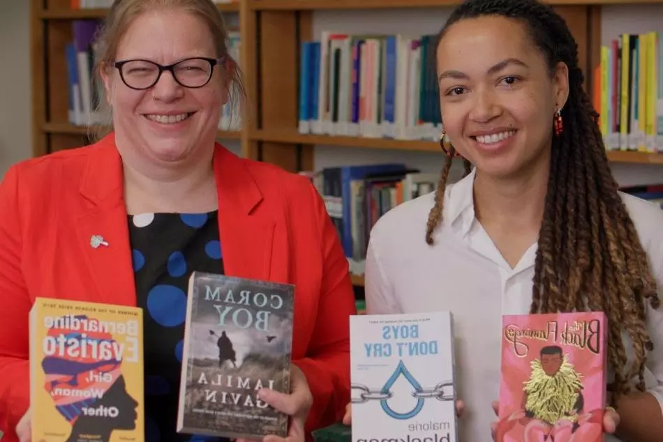 Dr Velda Elliott and Dr Zaahida Nabagereka sit side by side, smiling and holding books by authors of colour